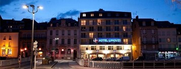 Um hotel com uma placa que diz 'HOTEL LIMOUZI' ao anoitecer.