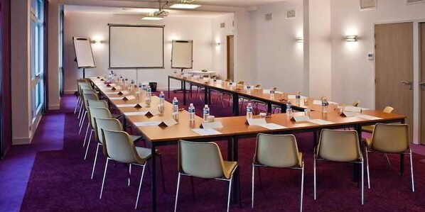 Un salón de conferencias con una larga mesa, varias sillas, una pantalla de proyector y una pizarra.