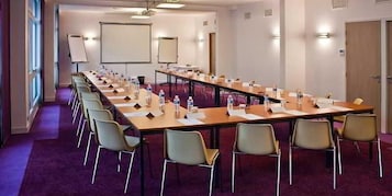 Uma sala de conferência com uma mesa comprida, várias cadeiras, uma tela de projetor e um quadro branco.