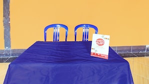 Une pièce avec une table bleue, deux chaises bleues et un panneau posé sur la table.