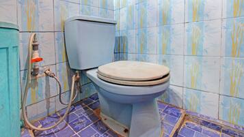 A bathroom with a toilet, a hose, and patterned tiles.
