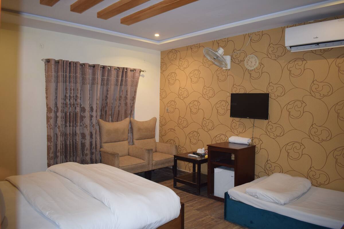 A hotel room with two beds, a chair, a small table, a TV, and an air conditioning unit.