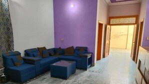 Ein Wohnzimmer mit einem blauen Ecksofa, einem Glastisch und einem gemusterten Vorhang.