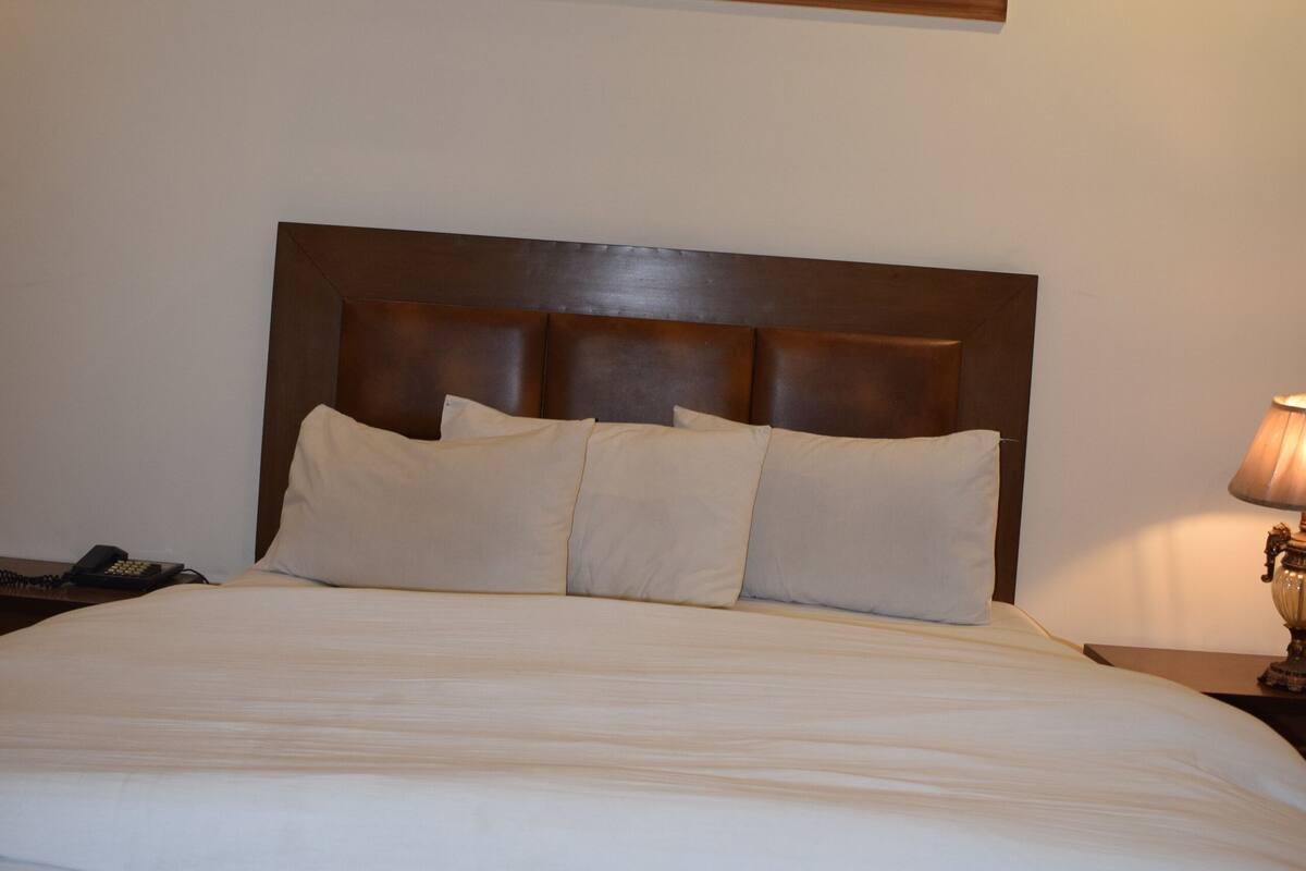 A hotel room with a large bed, wooden headboard, and a bedside table with a lamp.