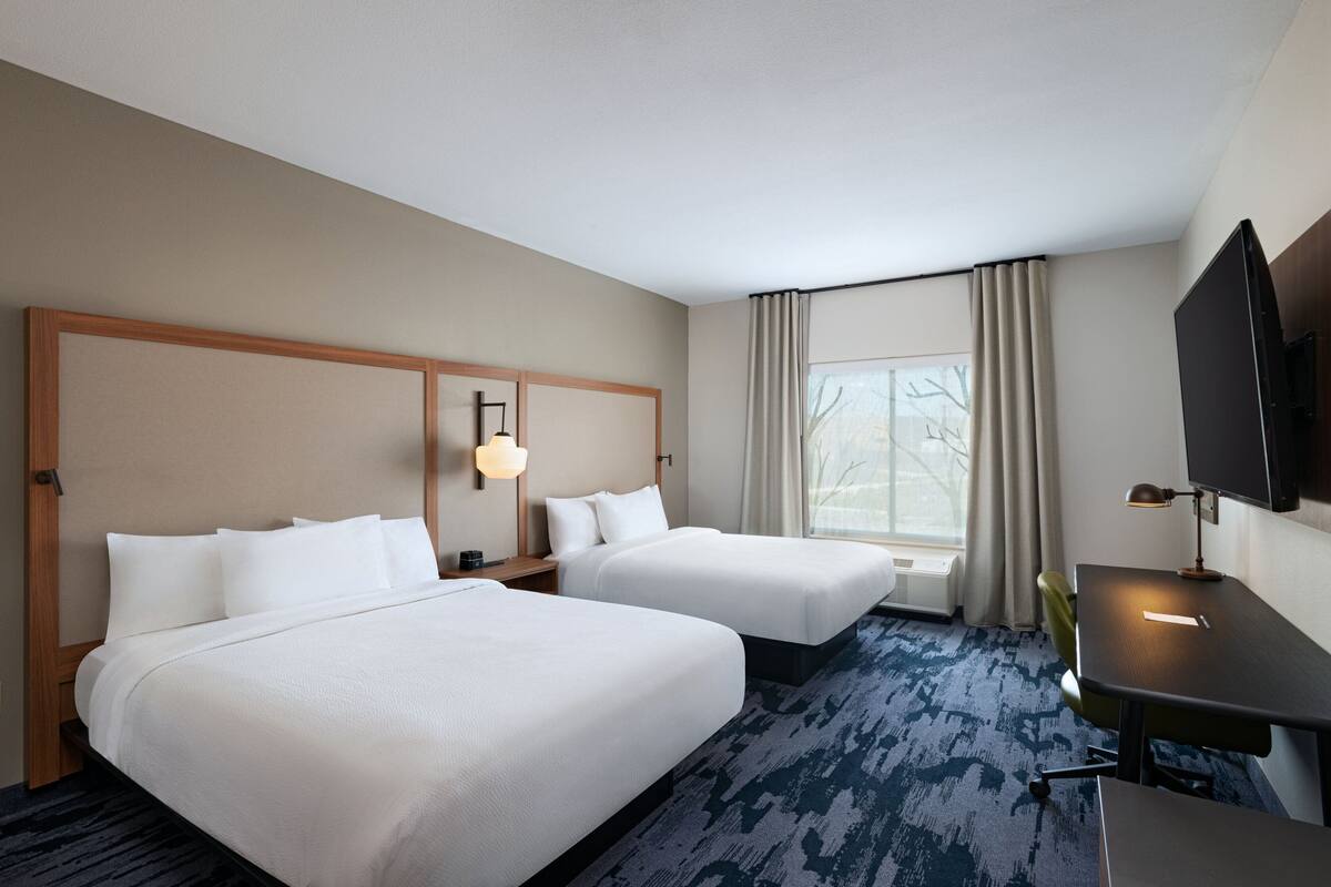 Une chambre d’hôtel avec deux lits, un bureau, une télévision et une fenêtre avec des rideaux.