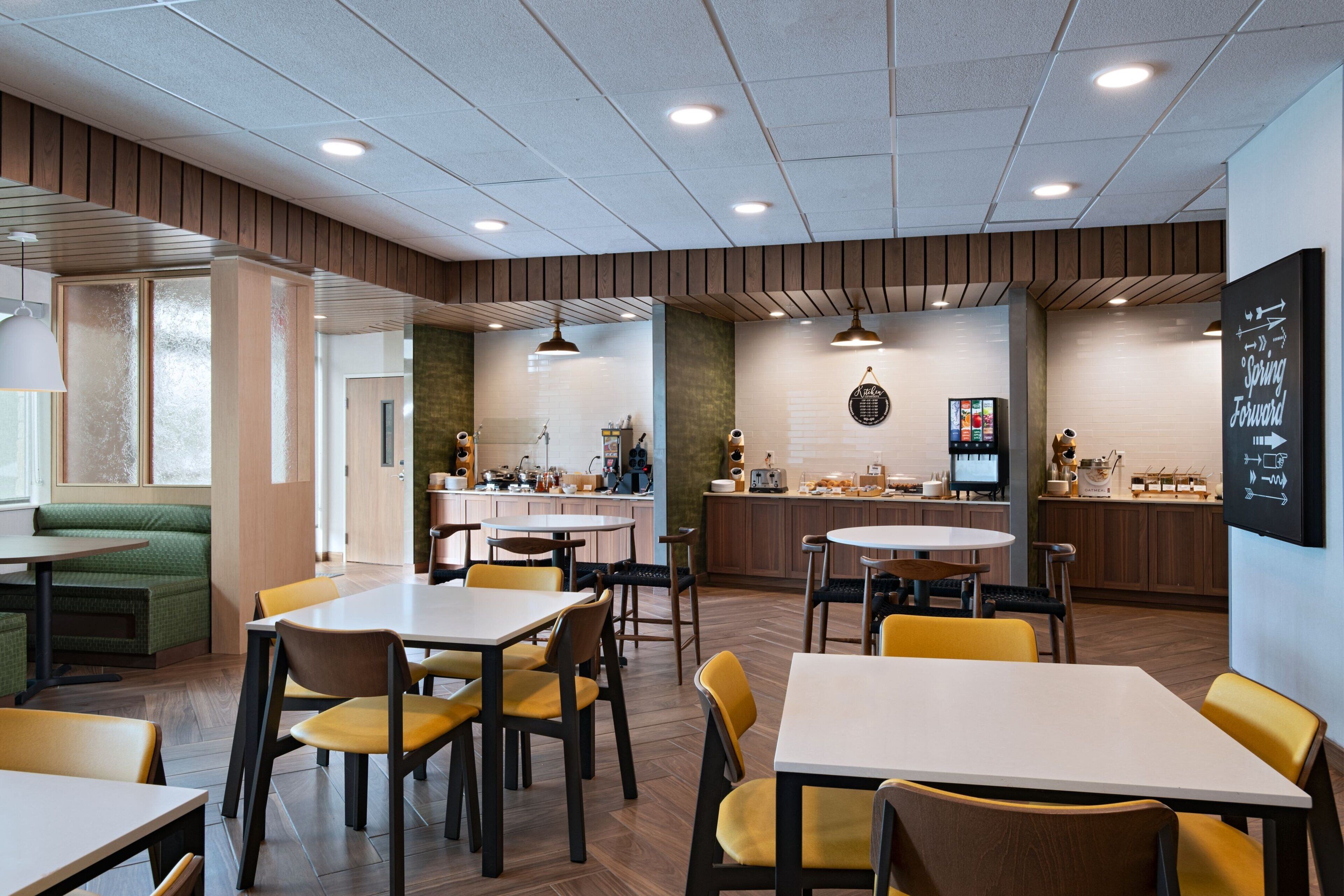 A modern restaurant with wooden accents, multiple dining areas, and a visible kitchen.
