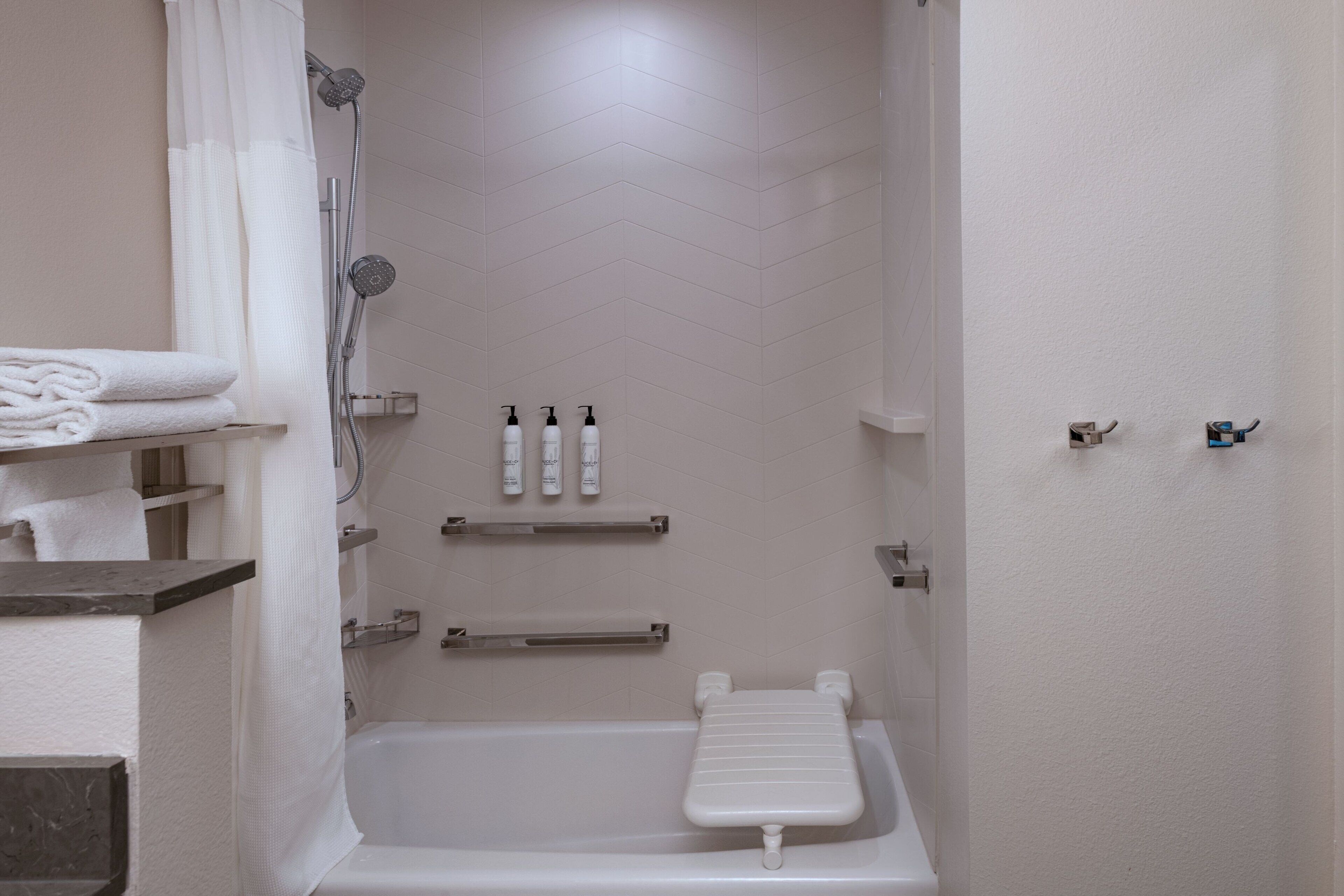 A modern bathroom with a bathtub, shower, and toilet. There are towels and toiletries on shelves.
