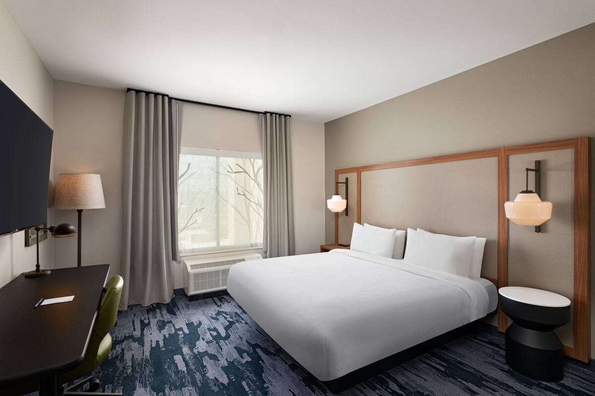 Une chambre d’hôtel avec un grand lit, un bureau, une chaise, une télévision et une fenêtre avec des rideaux.