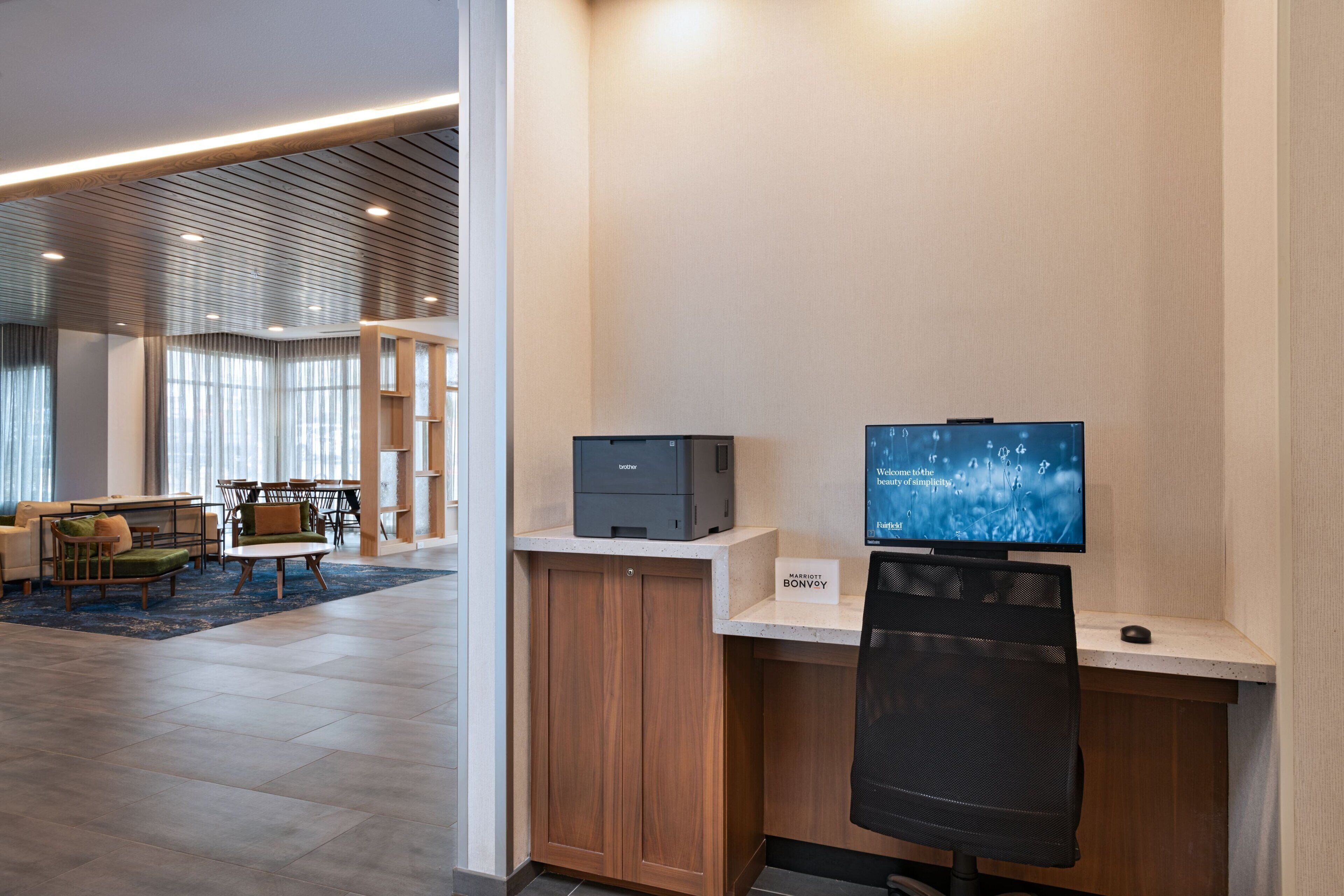 Un espace de bureau moderne avec un bureau, un ordinateur et un téléviseur. On aperçoit, au fond, un coin salon avec un canapé et des fauteuils.
