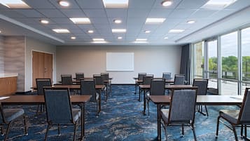 Un salón de conferencias con una gran mesa, sillas, una pantalla de proyector y vistas al exterior a través de amplias ventanas.