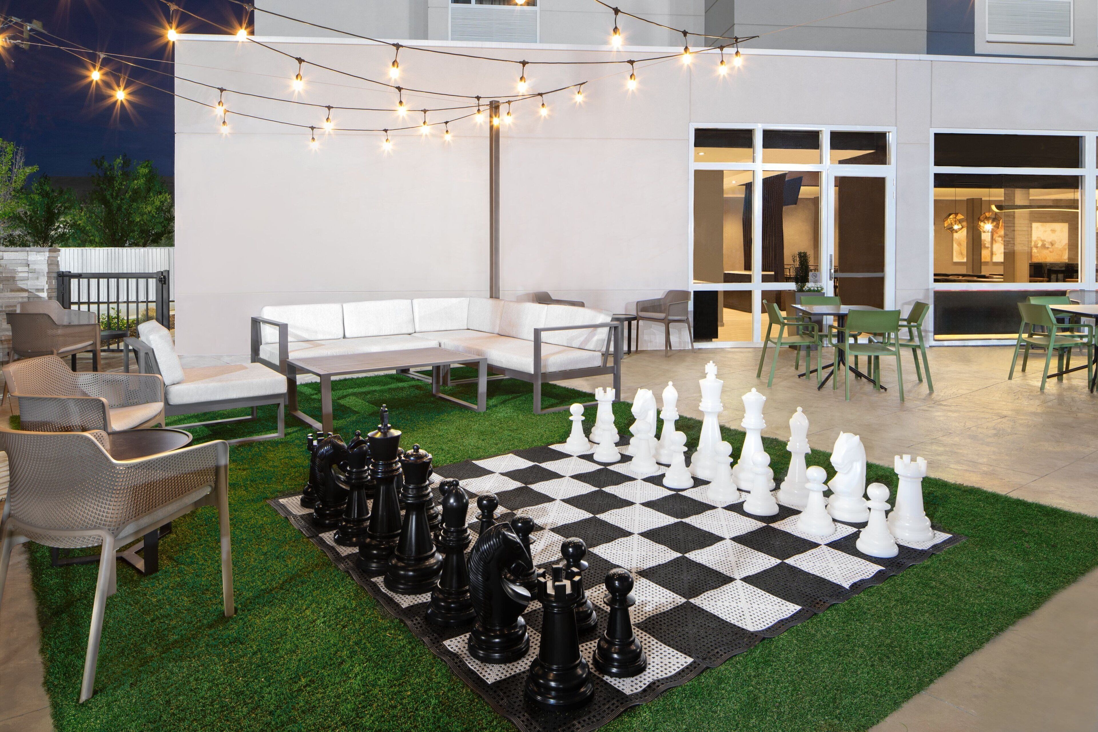 An outdoor patio with a chessboard, string lights, and seating.