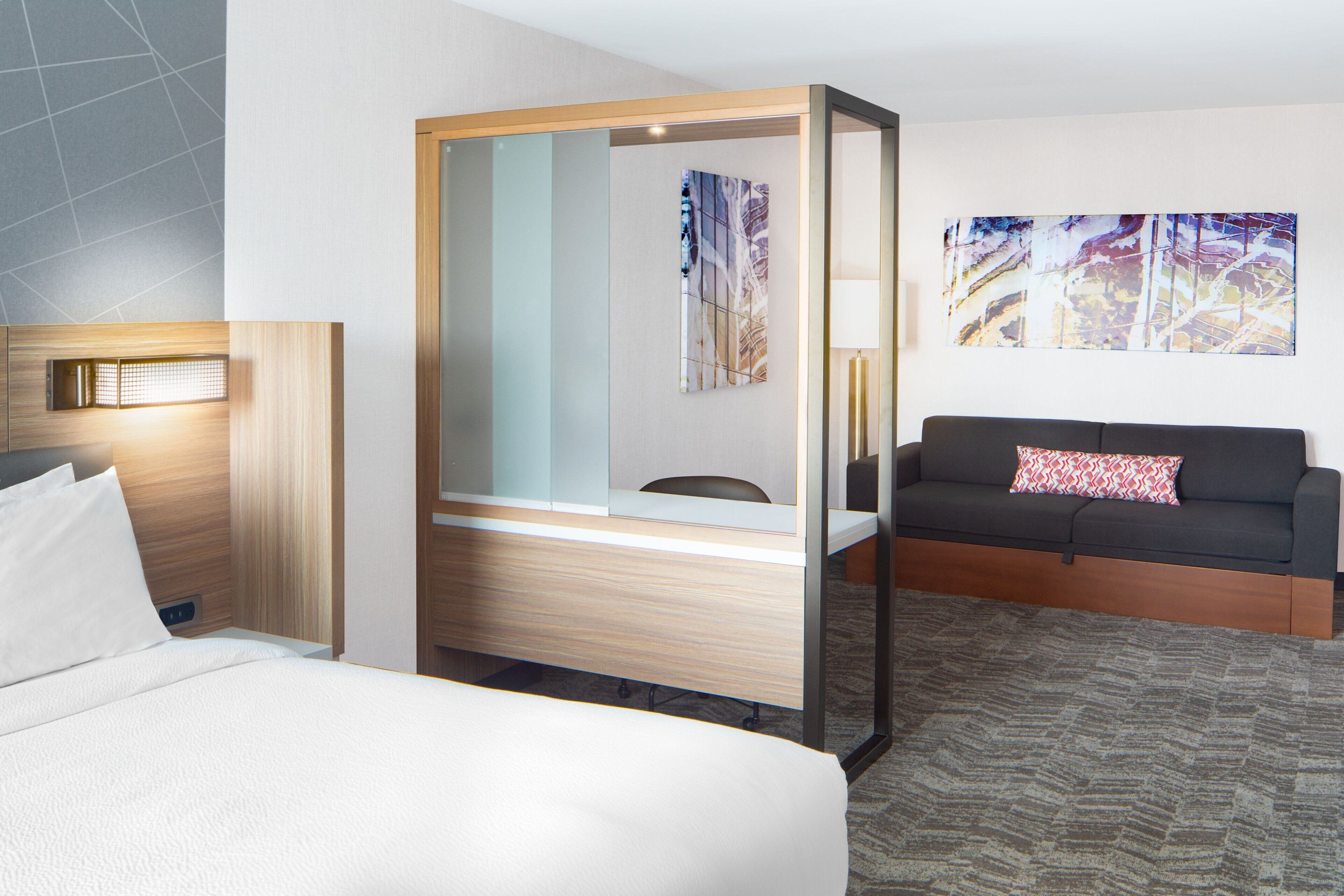 Une chambre d’hôtel avec un lit, un bureau, un canapé et un grand miroir.