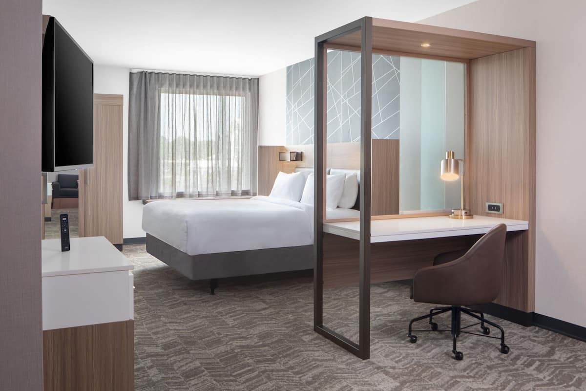 Ein modernes Hotelzimmer mit Bett, Schreibtisch, Stuhl, Fernseher und einem großen Spiegel.