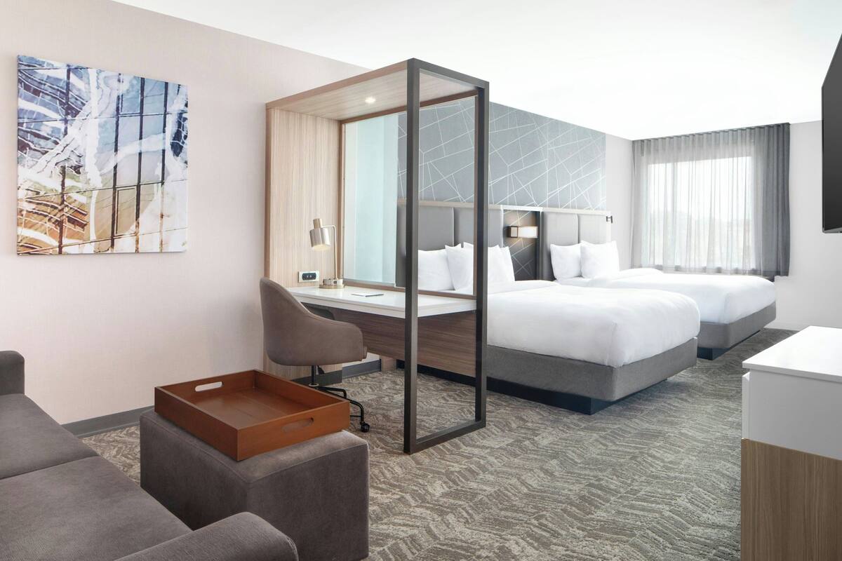 Ein Hotelzimmer im modernen Design mit einem großen Bett, einem Schreibtisch und einer Sitzecke mit Serviertisch.