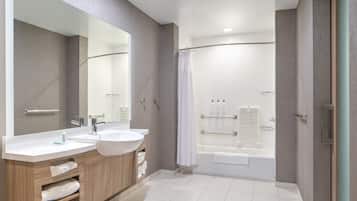 A modern bathroom with two sinks, a large mirror, a shower area, and a bathtub.