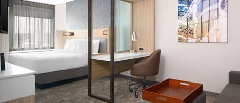 Una habitación de hotel con cama, escritorio, silla y un cuadro en la pared.