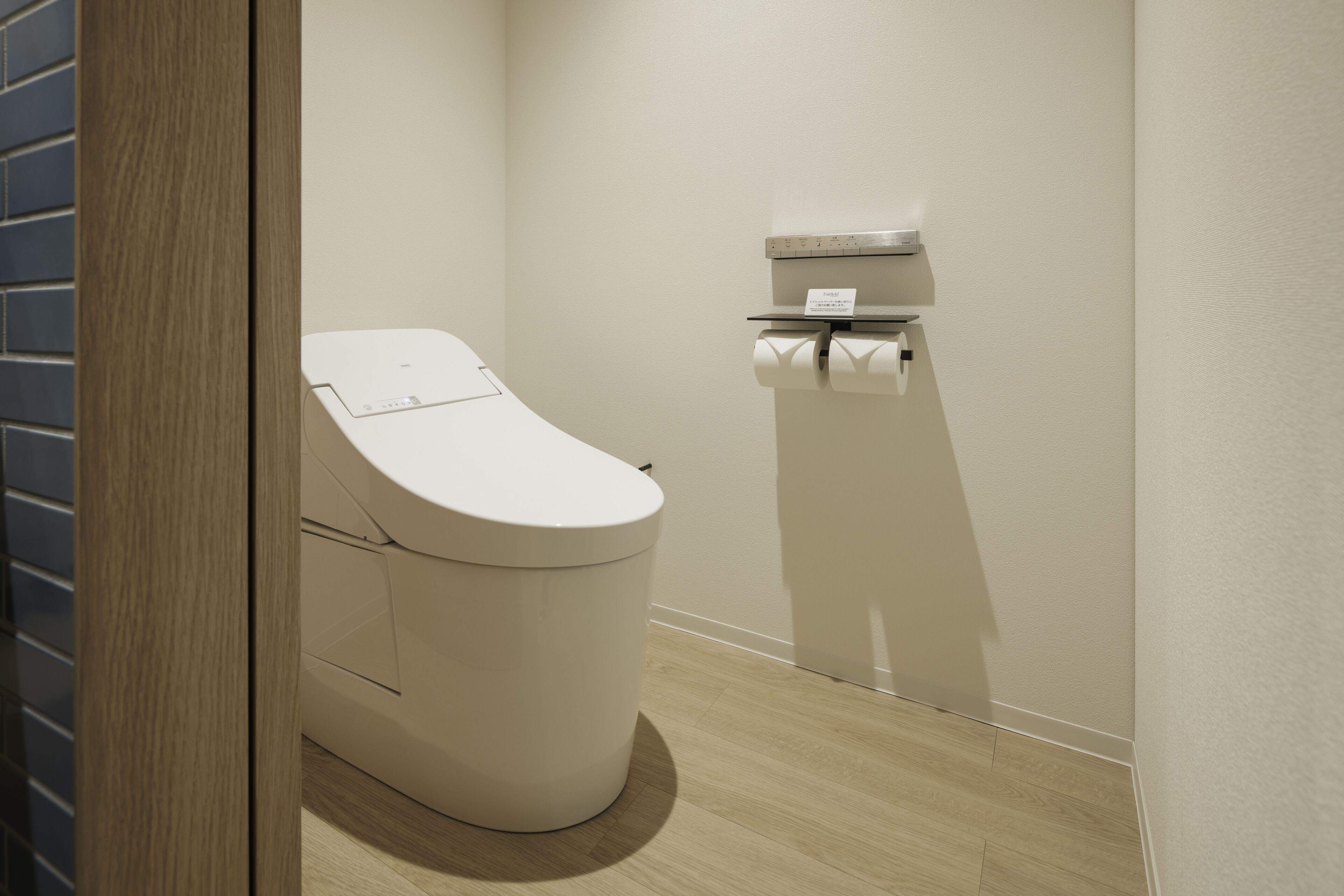 A modern bathroom with a toilet, a paper towel dispenser, and a wooden floor.