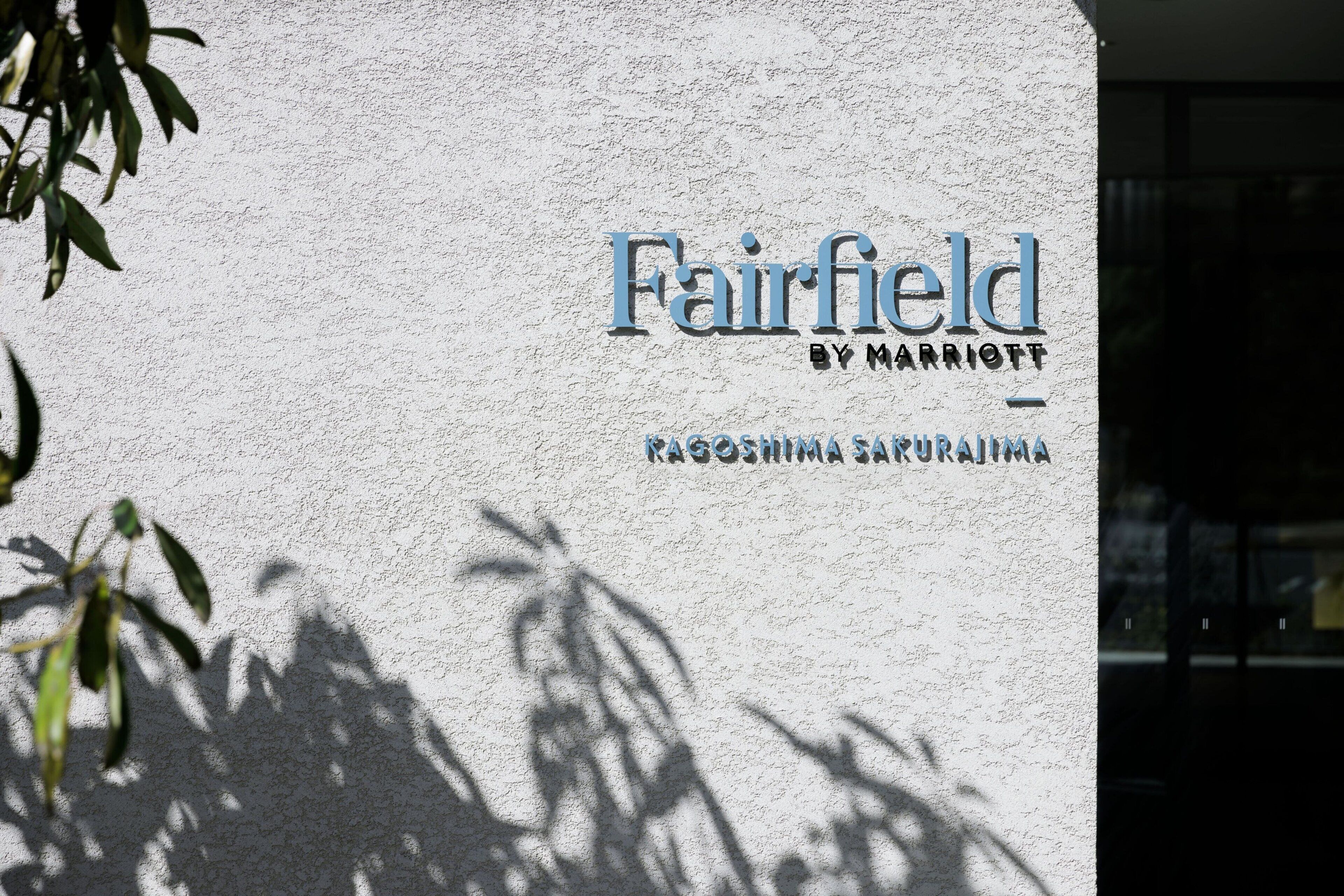 A sign for Fairfield by Marriott with a textured wall background and shadows of leaves.