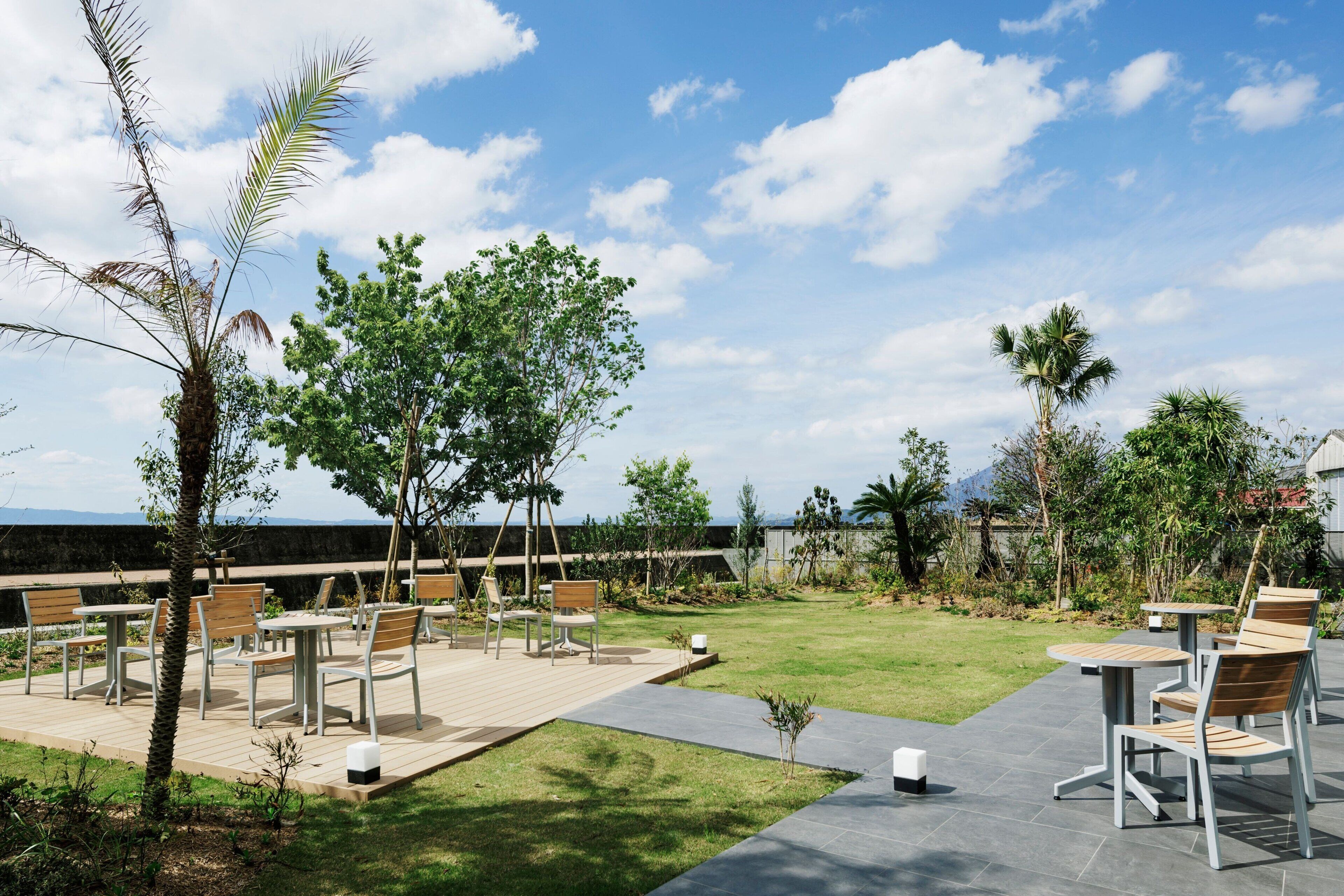 An outdoor patio area with tables and chairs, surrounded by greenery and palm trees.