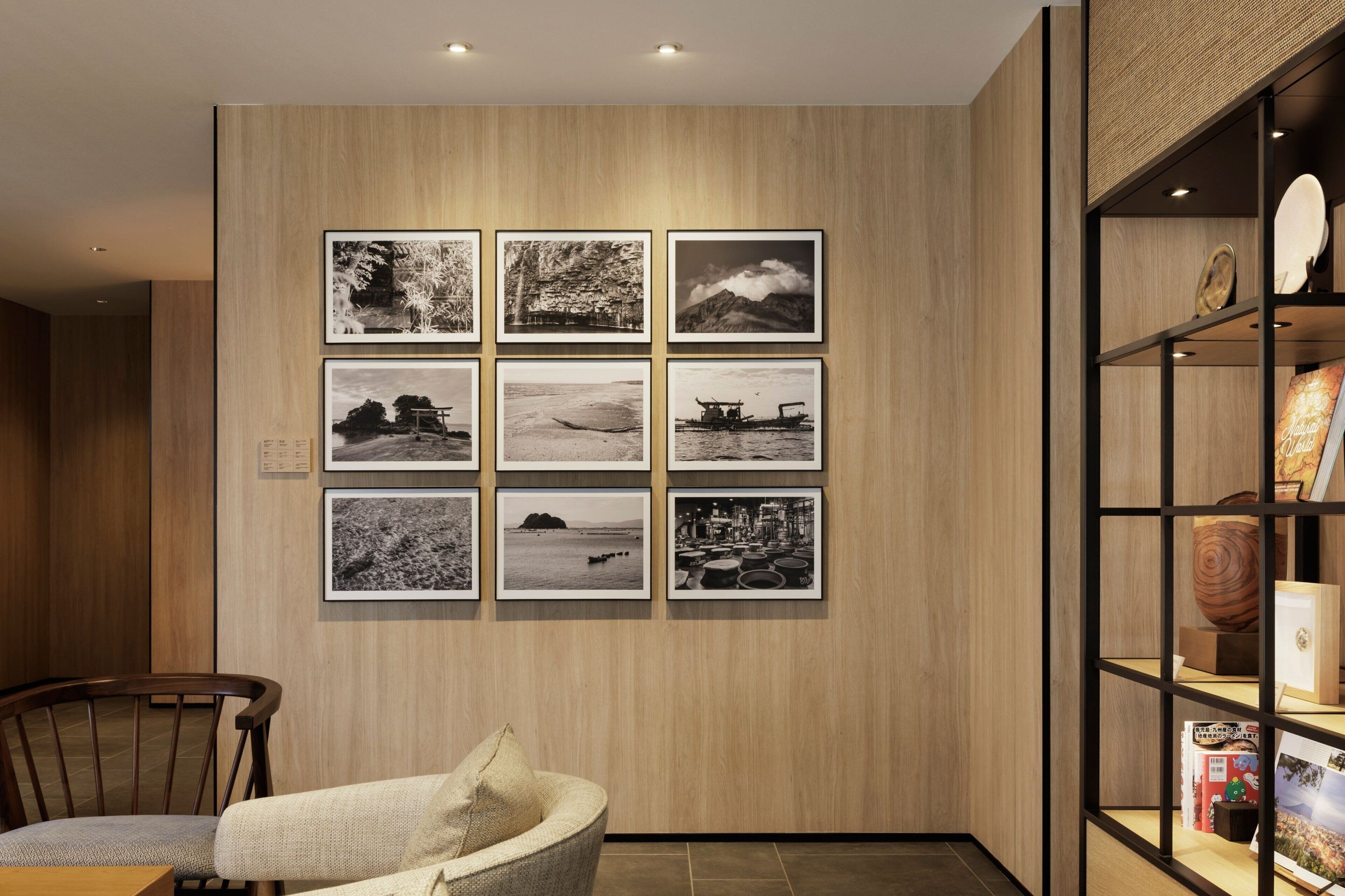A room with a wooden wall and a series of framed black and white photographs. There is a chair and a small table with a cushion.