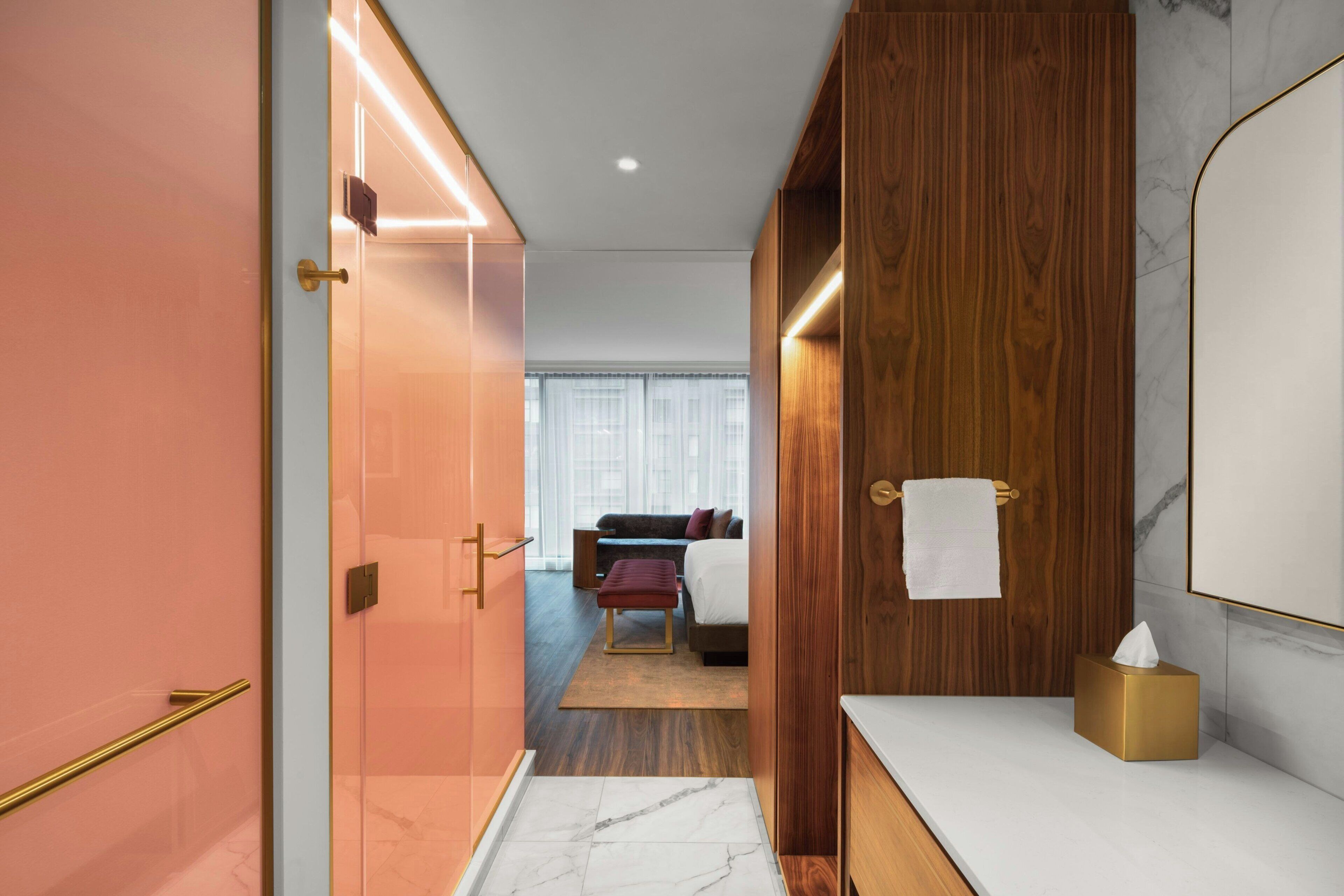 A modern hotel room with a wooden wardrobe, a marble-topped vanity, and a bed with a red bench.
