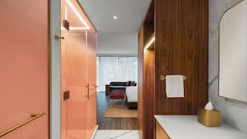A modern hotel room with a wooden wardrobe, a marble-topped vanity, and a bed with a red bench.