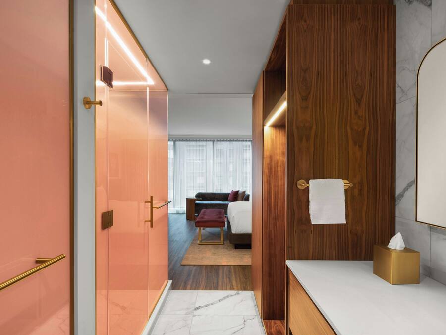 A modern hotel room with a wooden wardrobe, a marble-topped vanity, and a bed with a red bench.
