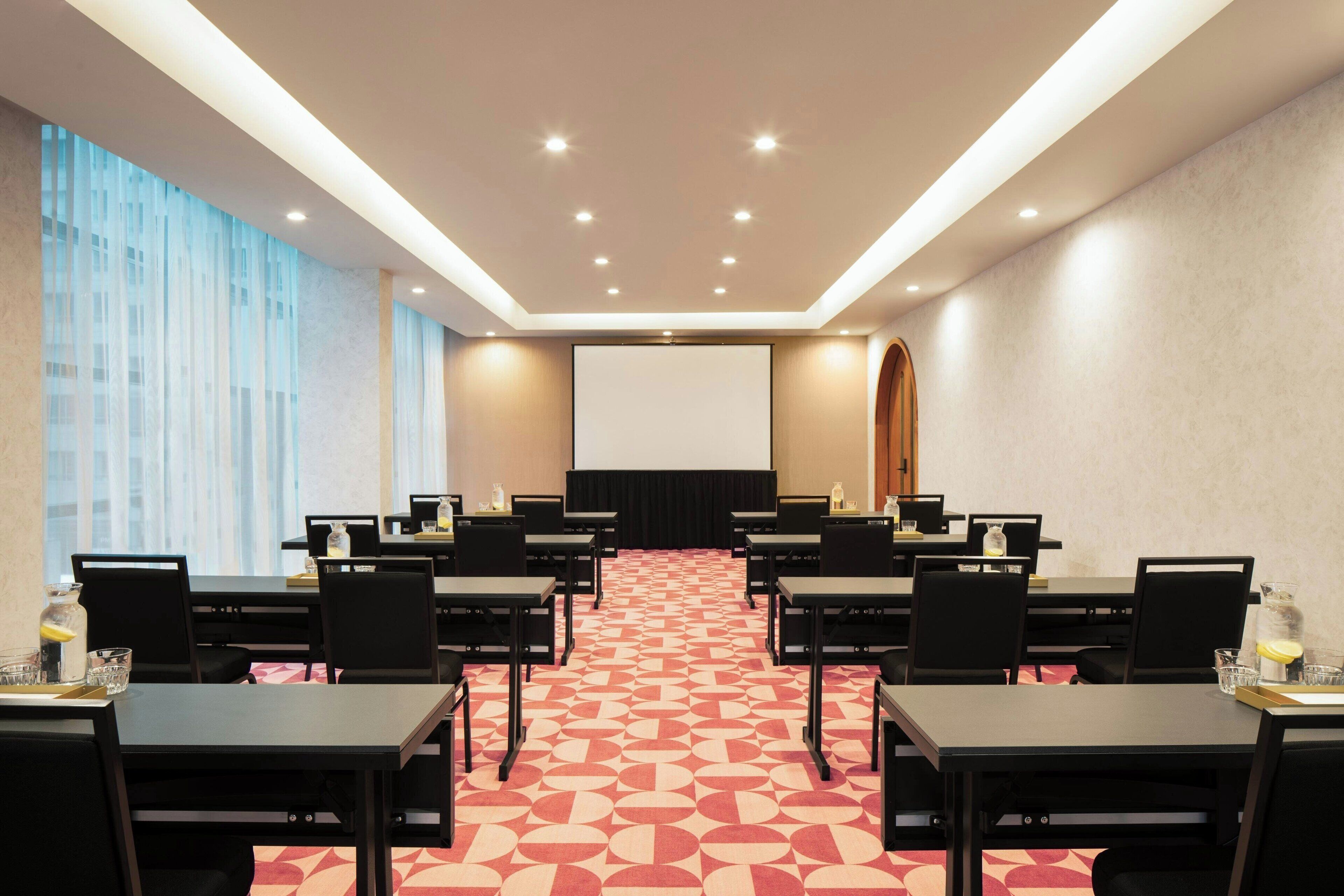 A conference room with a large screen, multiple tables, and chairs arranged for a meeting.