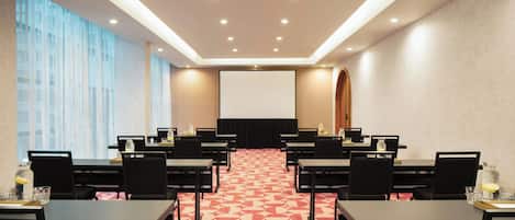 A conference room with a large screen, multiple tables, and chairs arranged for a meeting.