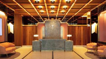 A hotel reception area with a central desk, two side lamps, and a large mirror on the right.