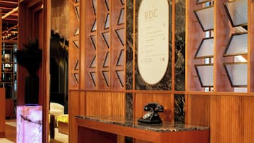 A reception desk with a wooden panel design, a marble counter, and a vintage telephone. A sign lists amenities including a reception, boutique, and commode.