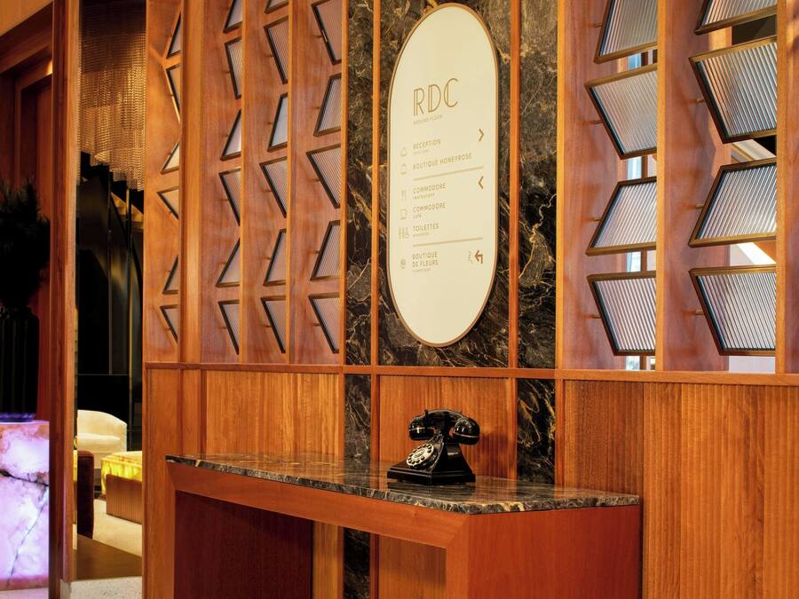 A reception desk with a wooden panel design, a marble counter, and a vintage telephone. A sign lists amenities including a reception, boutique, and commode.