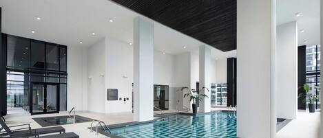 Ein moderner, überdachter Pool mit klarem Wasser, umgeben von schwarzen Bänken und einer großen Pflanze im Topf.