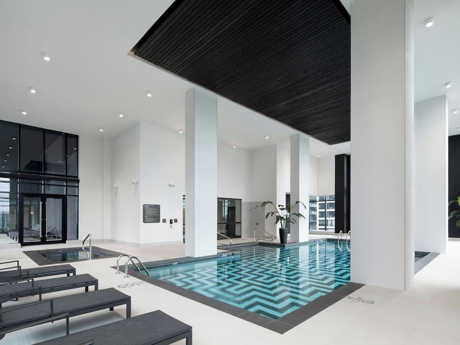 Ein moderner, überdachter Pool mit klarem Wasser, umgeben von schwarzen Bänken und einer großen Pflanze im Topf.