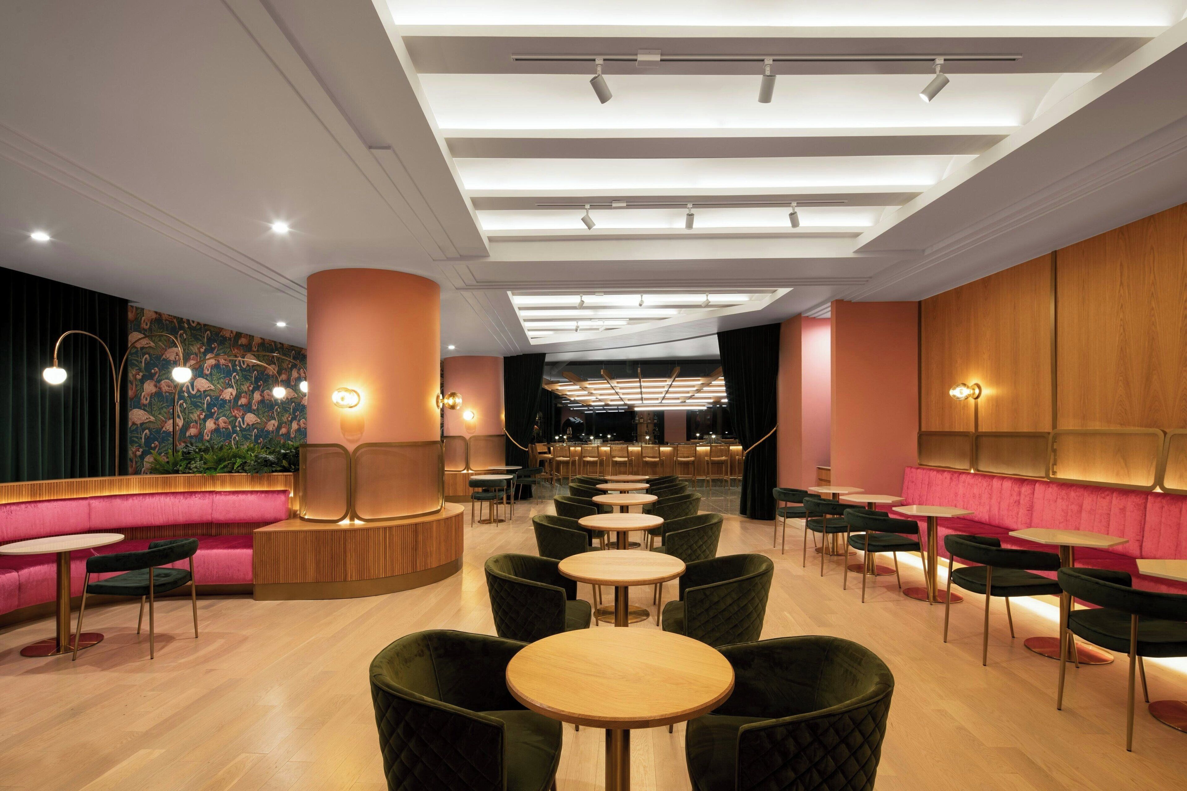 Interno di un ristorante moderno con un'area salotto centrale, diversi tavoli e un bar sullo sfondo.