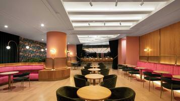 Interno di un ristorante moderno con un'area salotto centrale, diversi tavoli e un bar sullo sfondo.