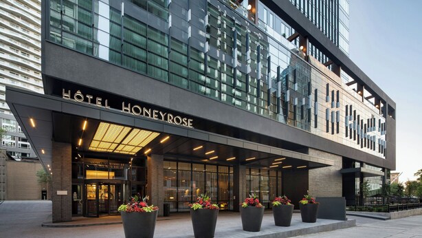 A modern hotel entrance with a glass facade, large potted plants, and a prominent sign reading "HOTEL HONEYROSE".