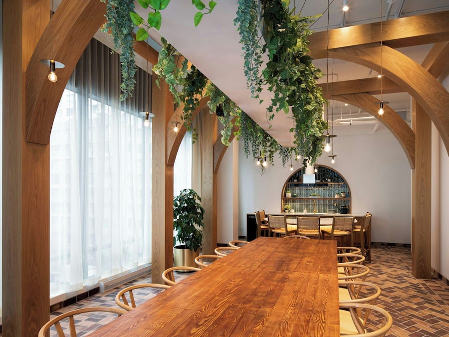Un salón de conferencias con una larga mesa de madera, sillas y plantas colgantes.