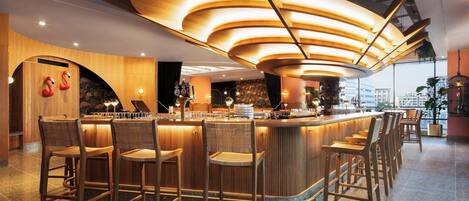 Eine moderne Bar mit einer gebogenen Holztheke, mehreren Barhocker und Blick auf die Stadt durch große Fenster.