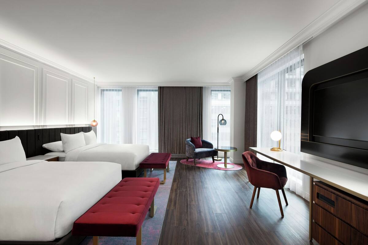 Habitación de hotel con dos camas, un escritorio, un televisor y un ventanal grande.