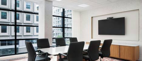 A conference room with a large table, six chairs, a projector screen, and large windows with a city view.