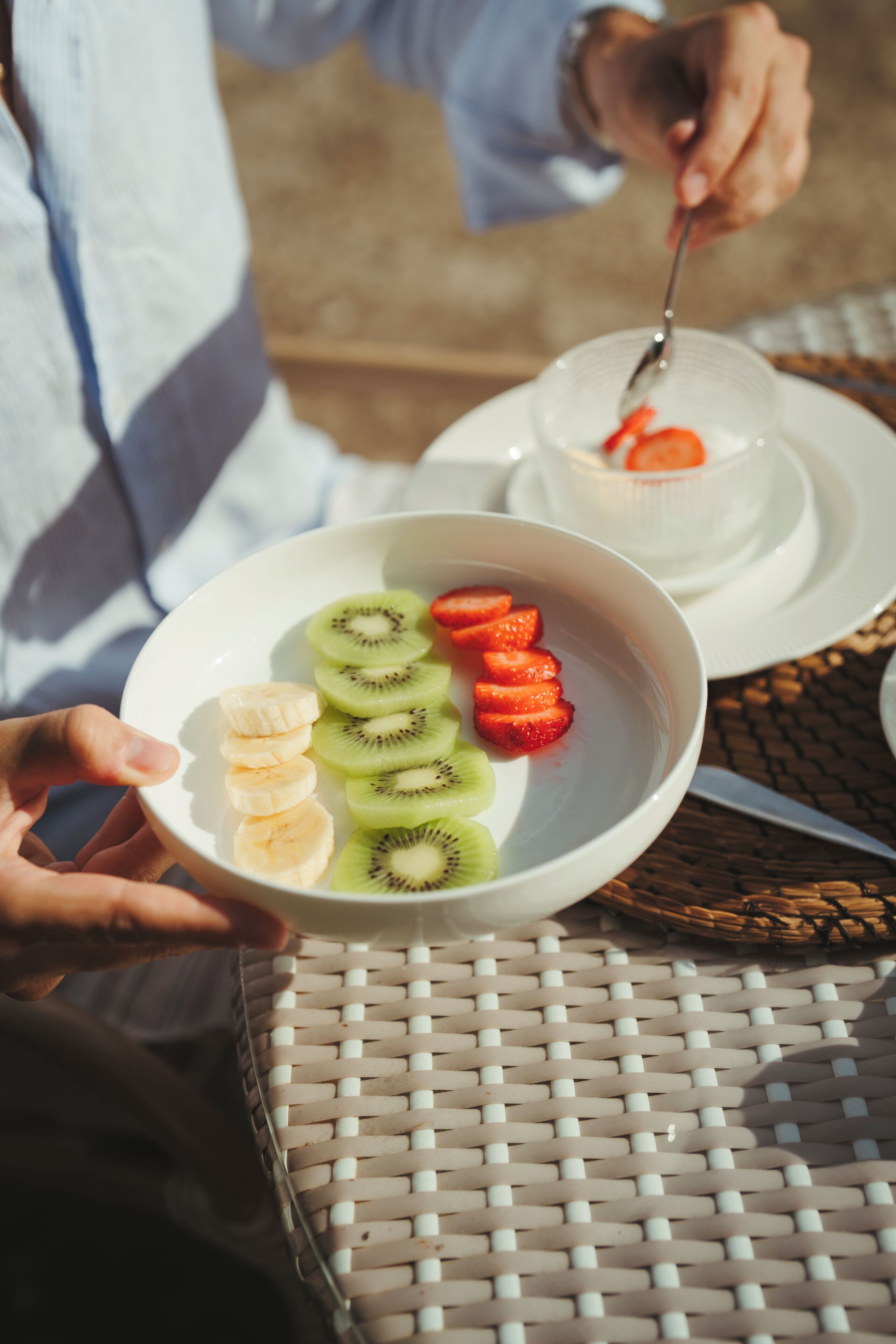A person holding a bowl with sliced fruits and a spoon.