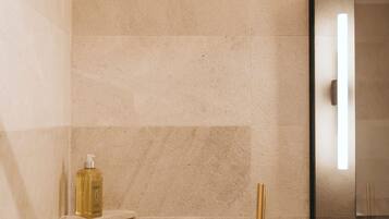 A modern bathroom with a shower, a gold-colored faucet, and a bottle of shampoo on a shelf.
