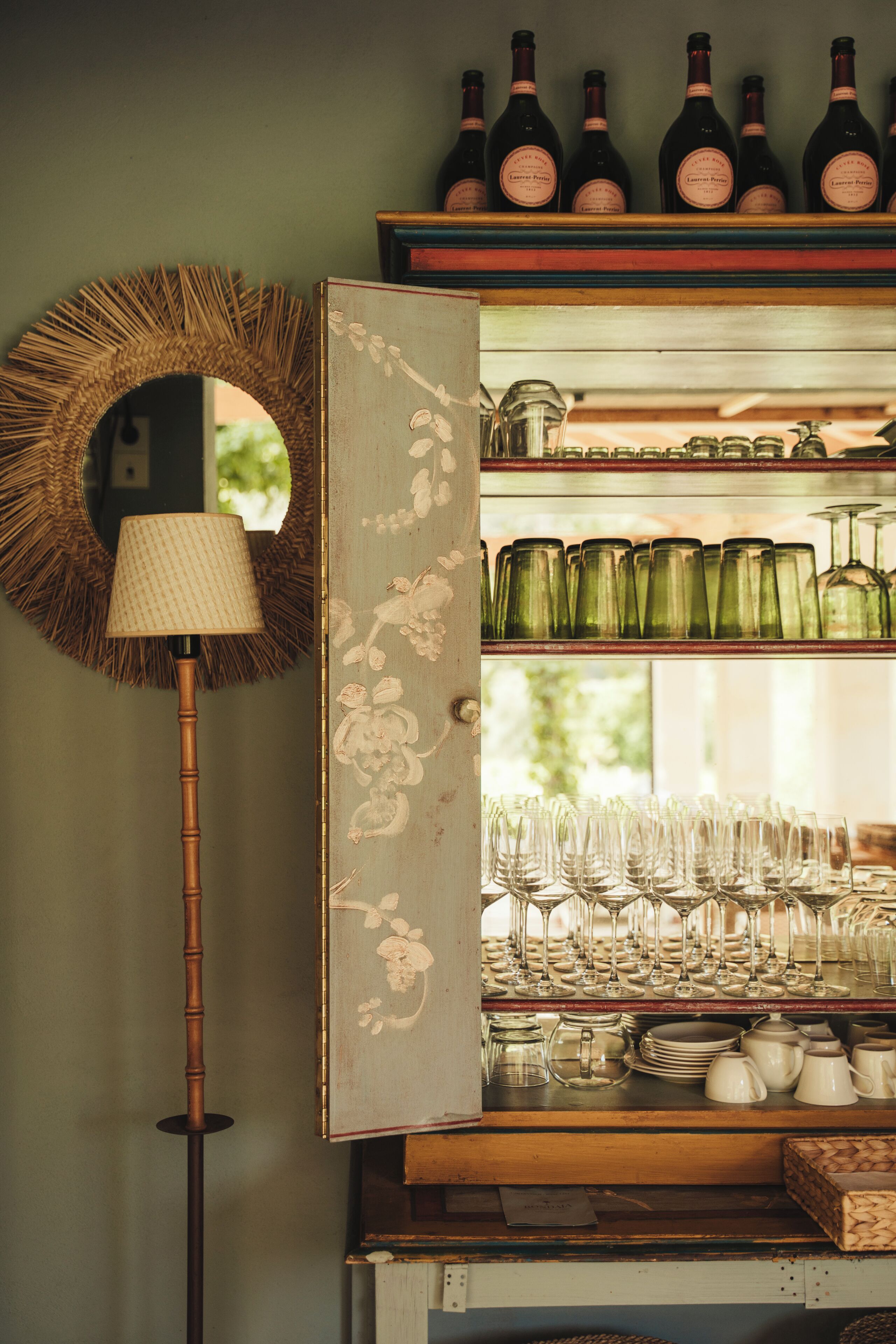 Una habitación con un espejo, una lámpara y un estante con botellas de vino y copas.