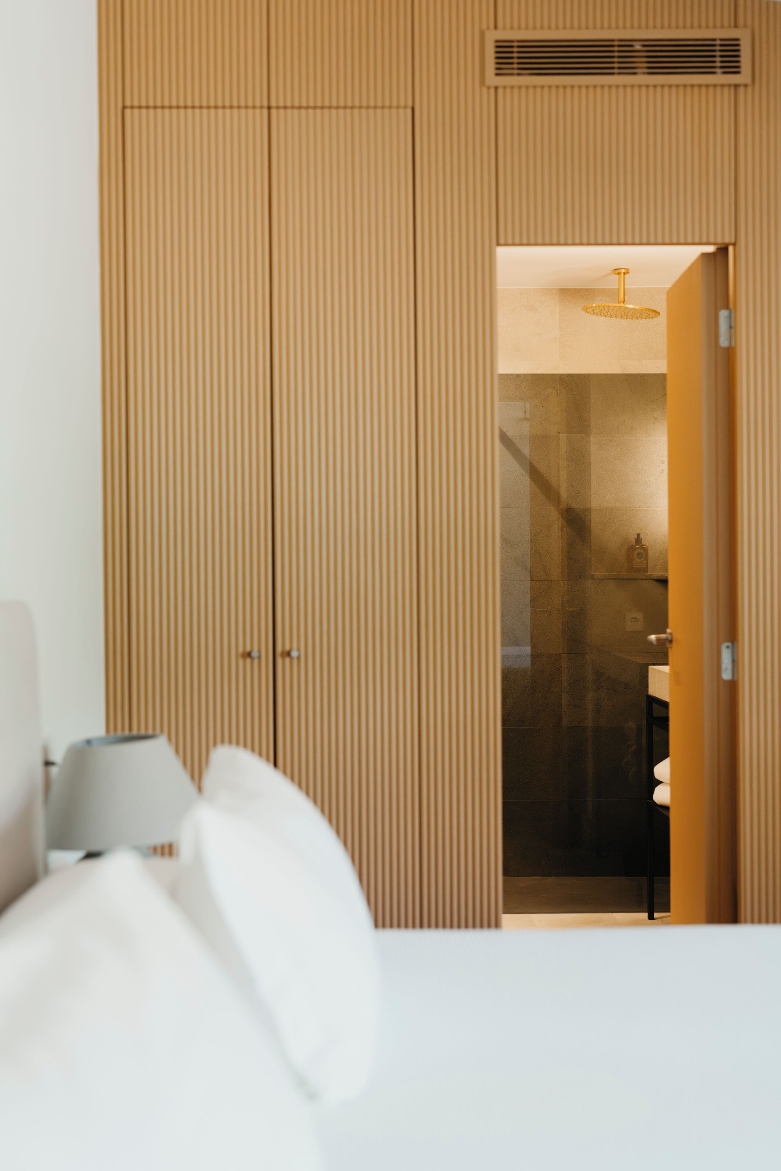 A hotel room with a bed, a bedside table, a lamp, and a wardrobe with a mirror.