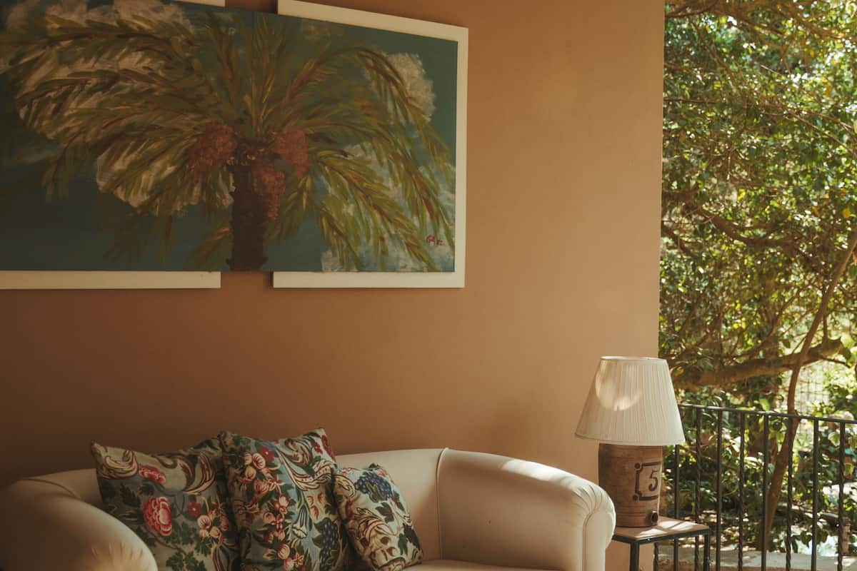 A cozy living room with a beige sofa, floral cushions, a wooden coffee table, and a painting of a palm tree.
