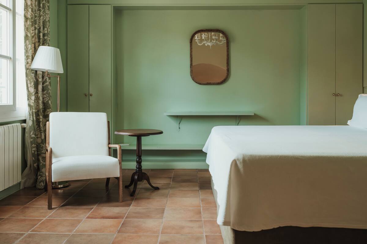 A room with a bed, a chair, a small table, a mirror, and a radiator.