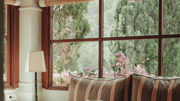 A cozy room with a wooden bench, a table with a glass, and a window with a view of trees and flowers. - Rondaia Boutique Vineyard Stay – Mallorca, Tramuntana (Esporles)