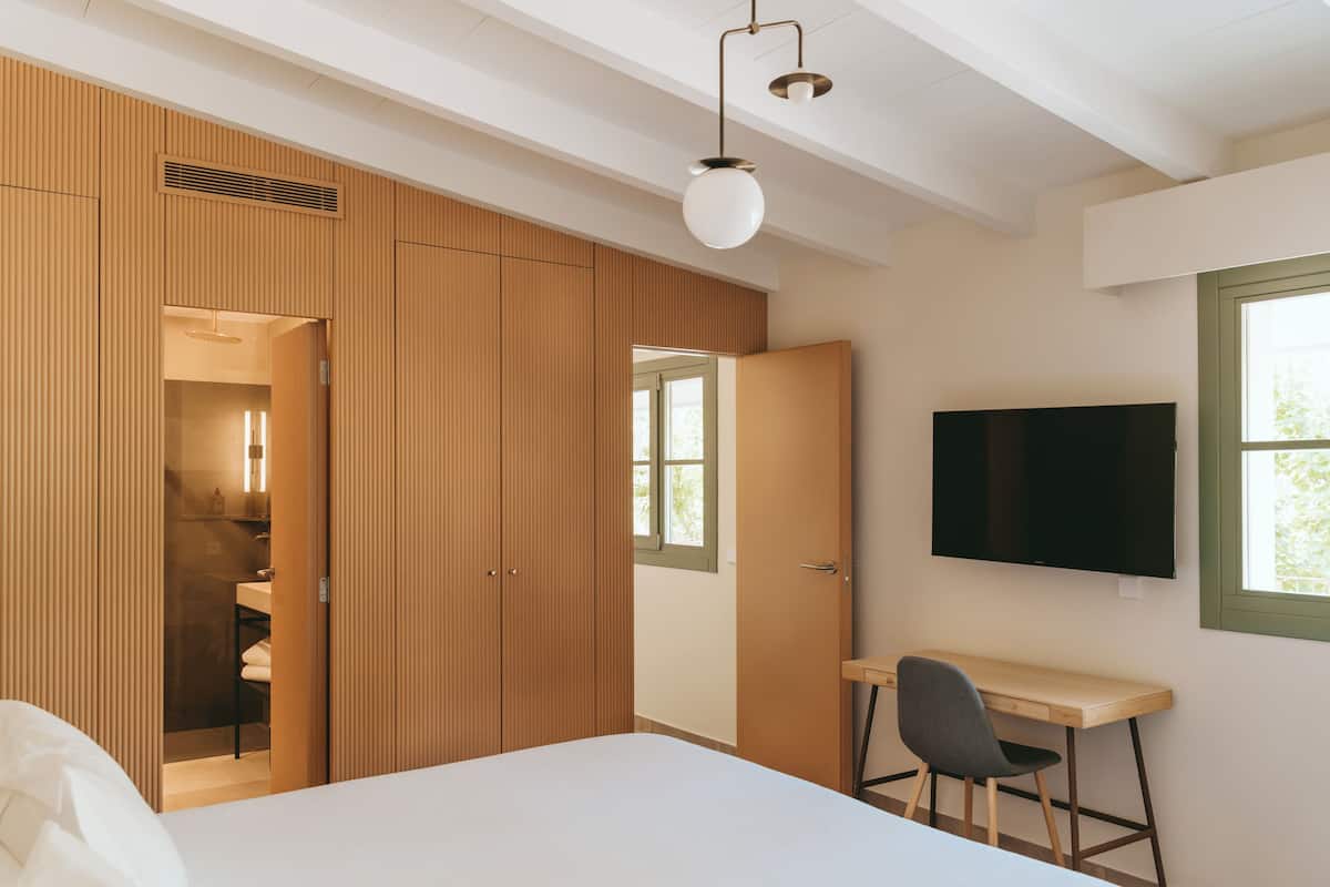 A bedroom with a bed, a desk, and a TV. There is a wardrobe and a window.