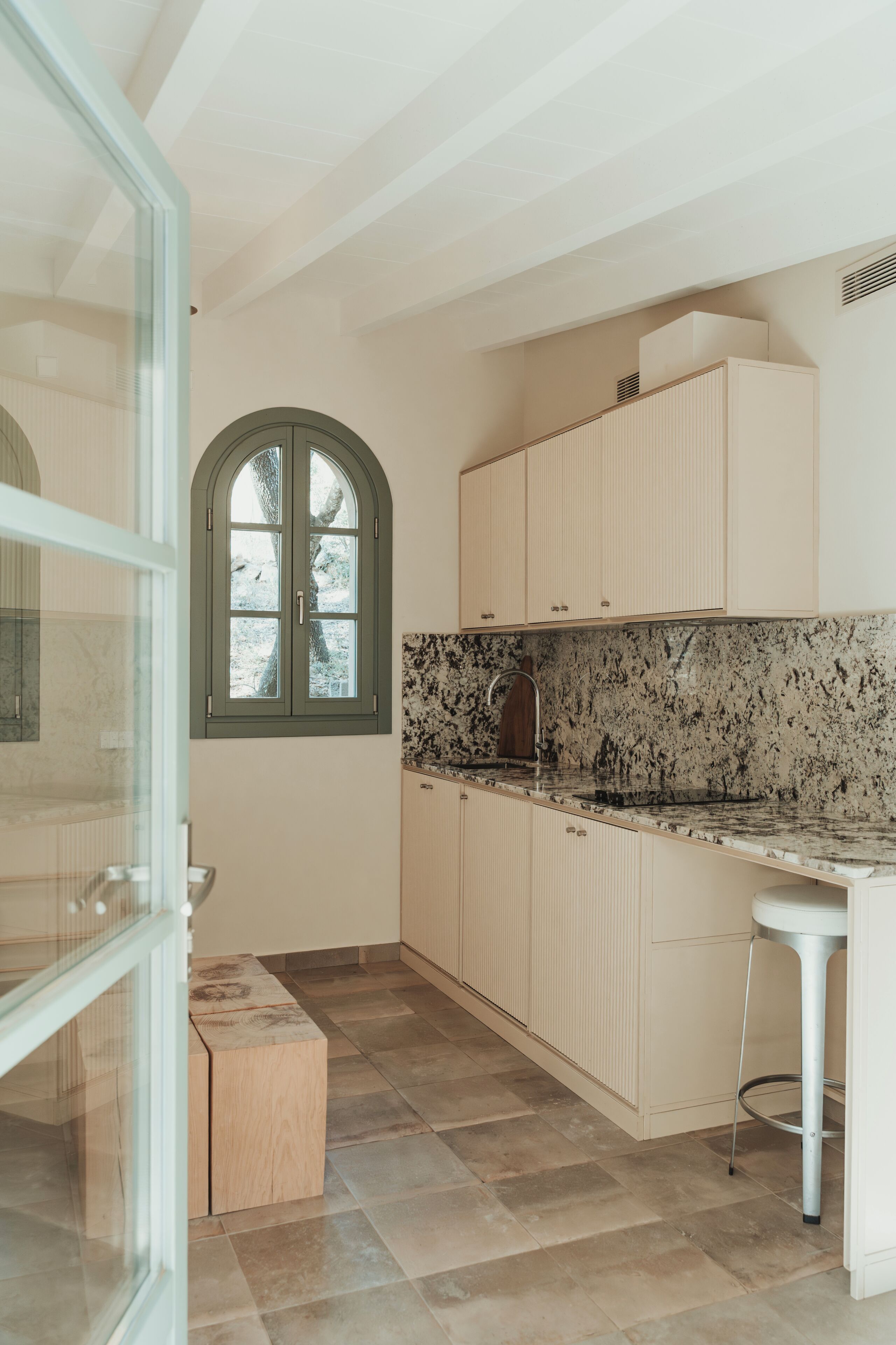 A kitchen with a marble countertop, wooden cabinets, and a window with a view of trees.